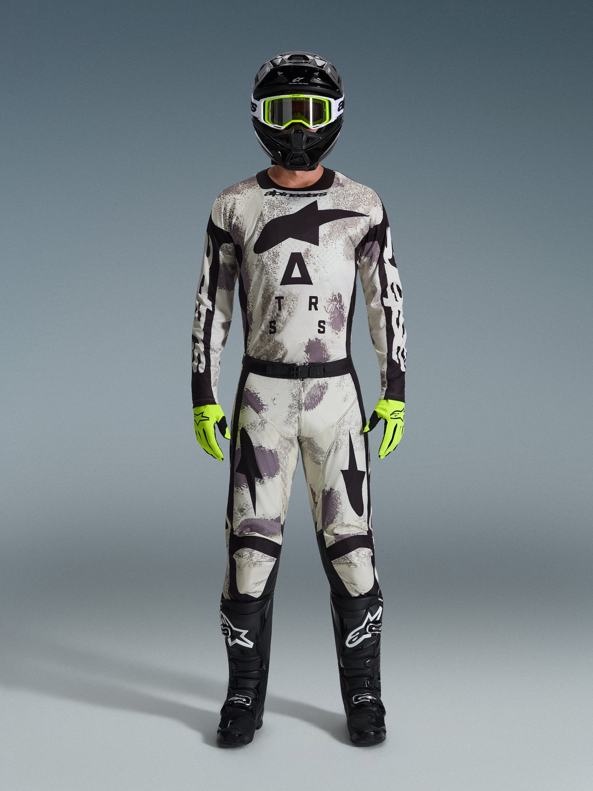 Motocross-Fahrer in kompletter Rennausrüstung, Alpinestars 2026 Racer Lahnd Hose und passendes Jersey in Sand Camo Grau, schwarzer Helm mit neongelber Brille, leuchtend neongelbe Handschuhe und schwarze Stiefel, abgestimmtes Profi-Outfit für den Offroad-Rennsport