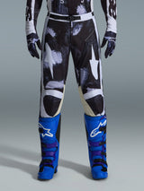 Alpinestars 2026 Racer Lahnd Pants, Motocross Pants, Iron Camo, worn with matching camouflage gloves and bright blue and purple boots, featuring stylized white star graphics on a dark camo pattern, technical magnetic buckle closure, professional off-road racing gear.