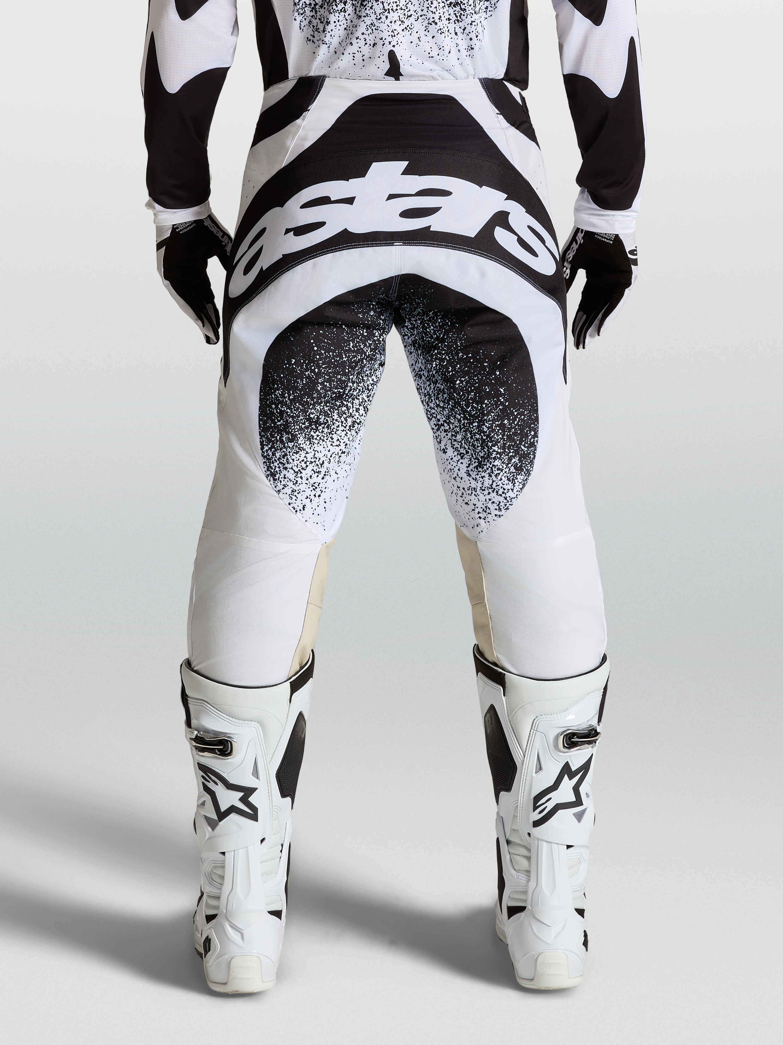 Alpinestars Techstar Swan Hose, Motocross-Hose in Schwarz und Weiß, Rückansicht mit großem Astar-Logo am Gesäß, Babel-Kniekonstruktion, getragen mit weißen Motorradstiefeln für den Offroad-Einsatz.