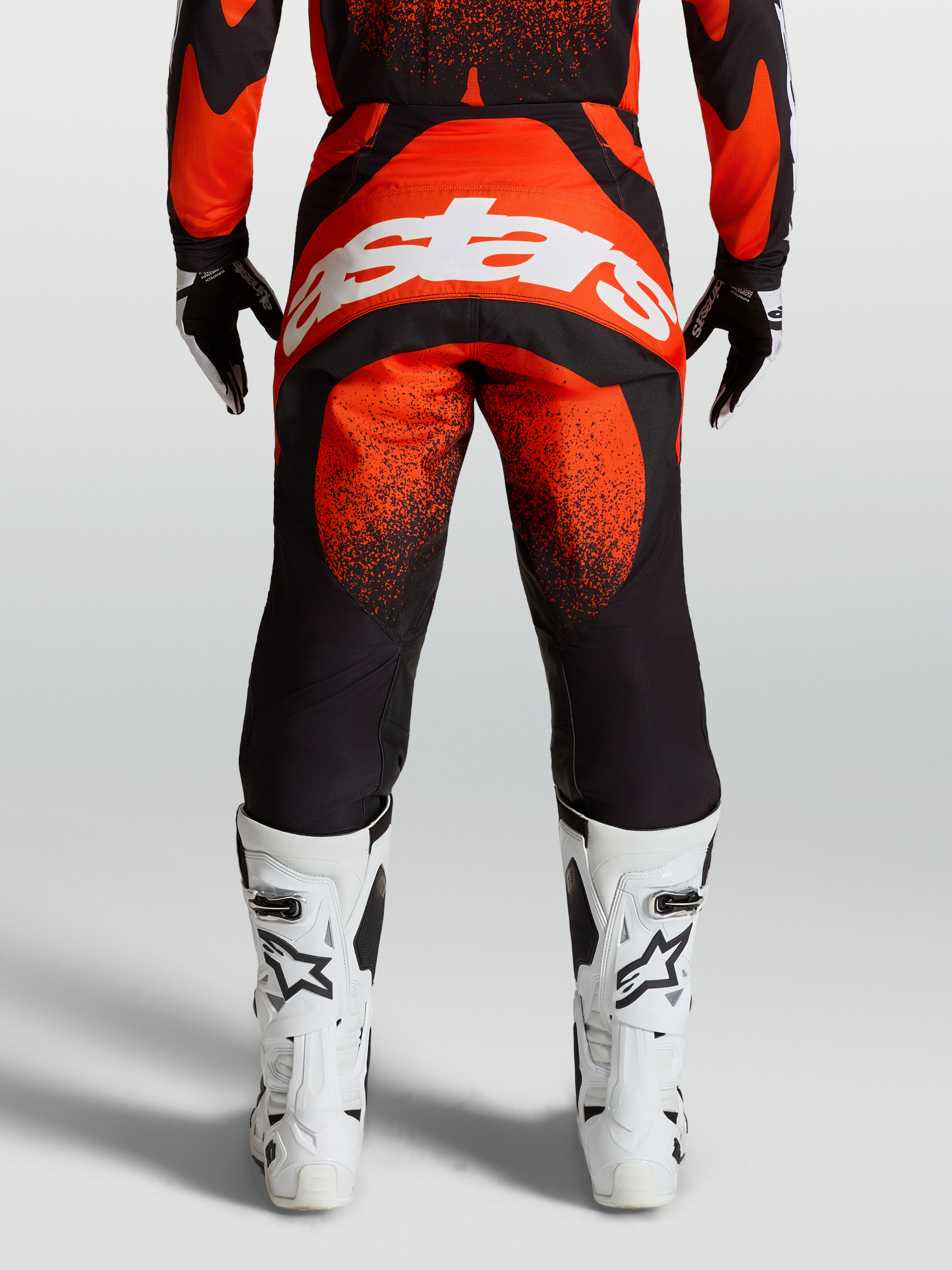Alpinestars Techstar Swan Hose, MX-Hose in Rot und Schwarz, Rückansicht am Model mit weißem Astars-Logo und weißen Rennstiefeln, Offroad-Motocross-Ausrüstung