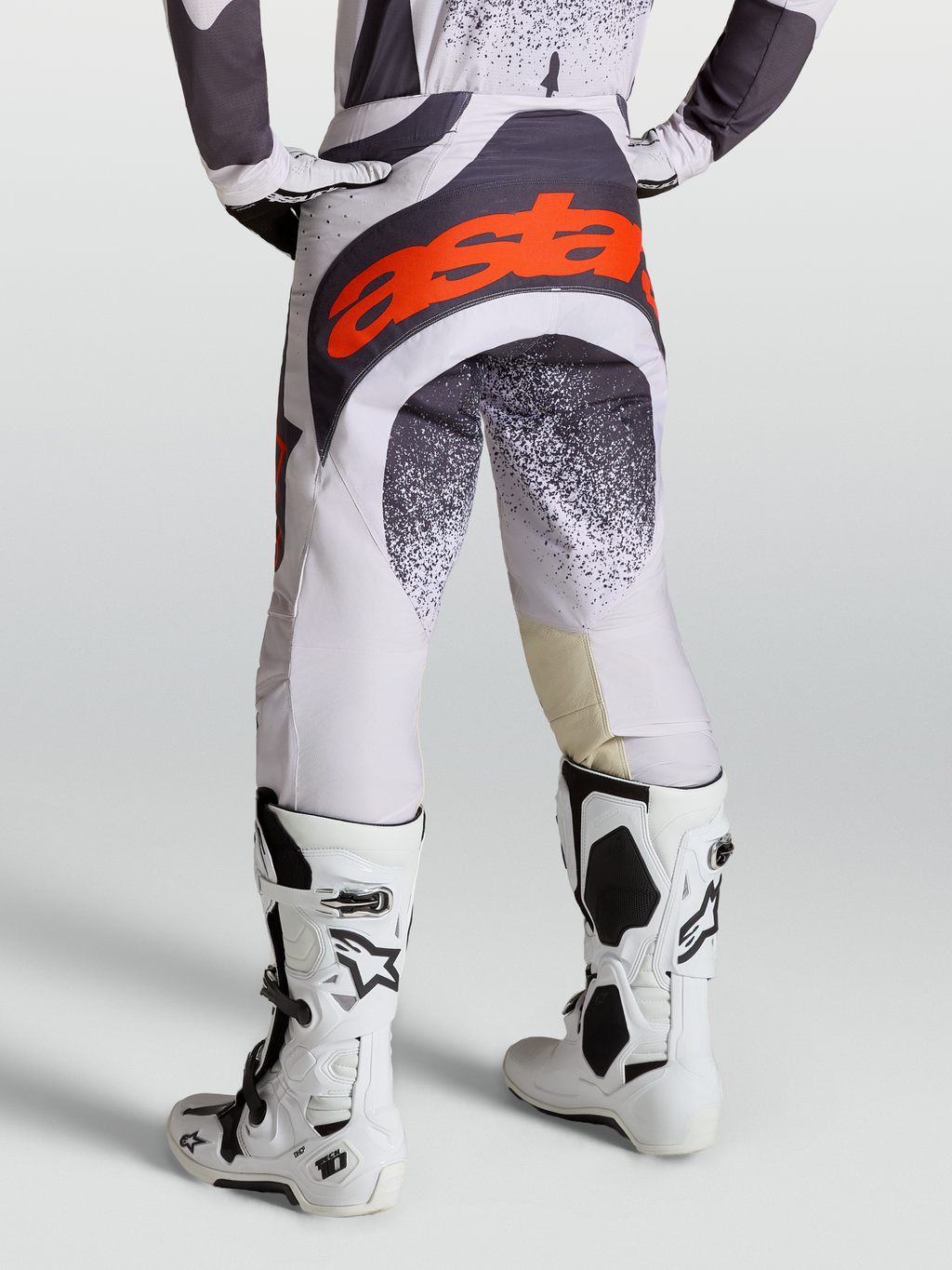 Alpinestars Techstar Swan Hose, Motocross-Hose für Herren, Helllila und Dunkelgrau mit roten Akzenten, kombiniert mit weißen Tech 10 Stiefeln, Rückansicht.