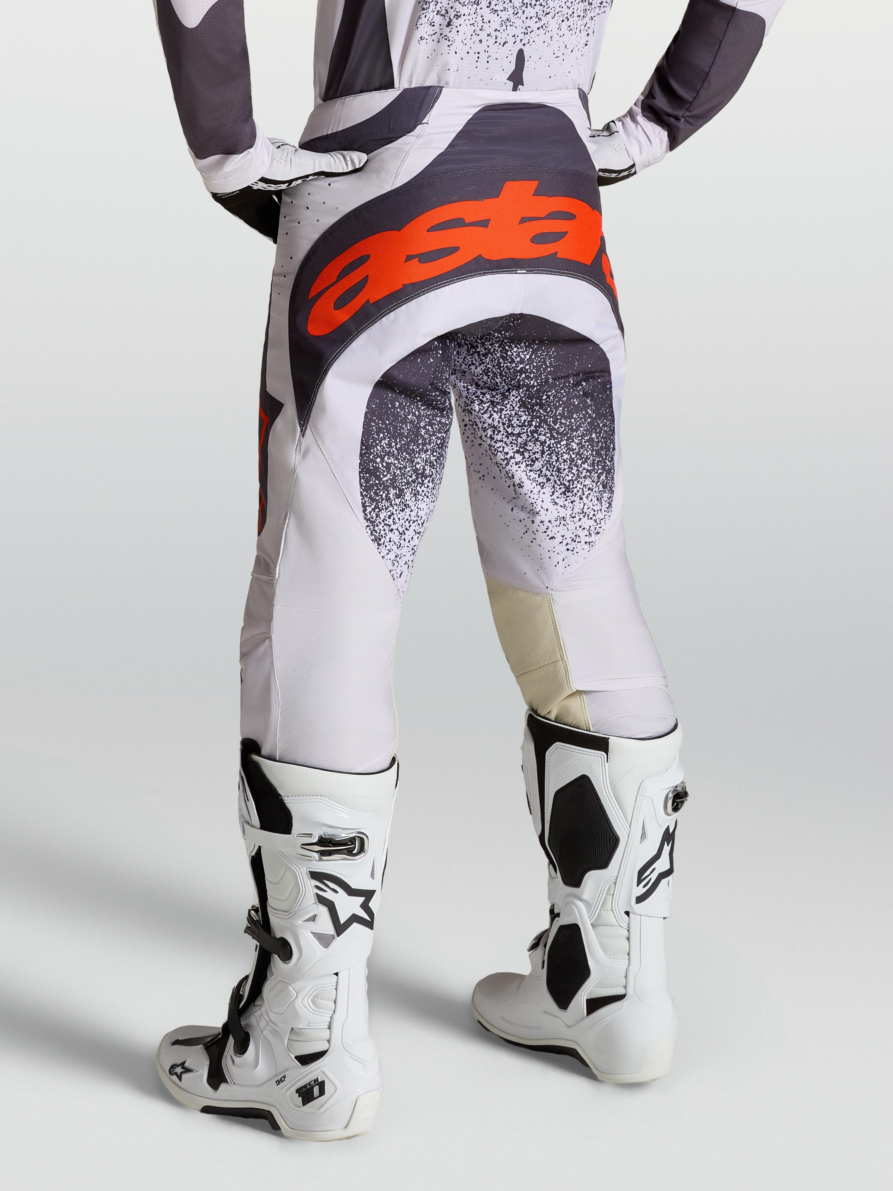 Alpinestars Techstar Swan Hose, Motocross-Hose für Herren, Helllila und Dunkelgrau mit roten Akzenten, kombiniert mit weißen Tech 10 Stiefeln, Rückansicht.