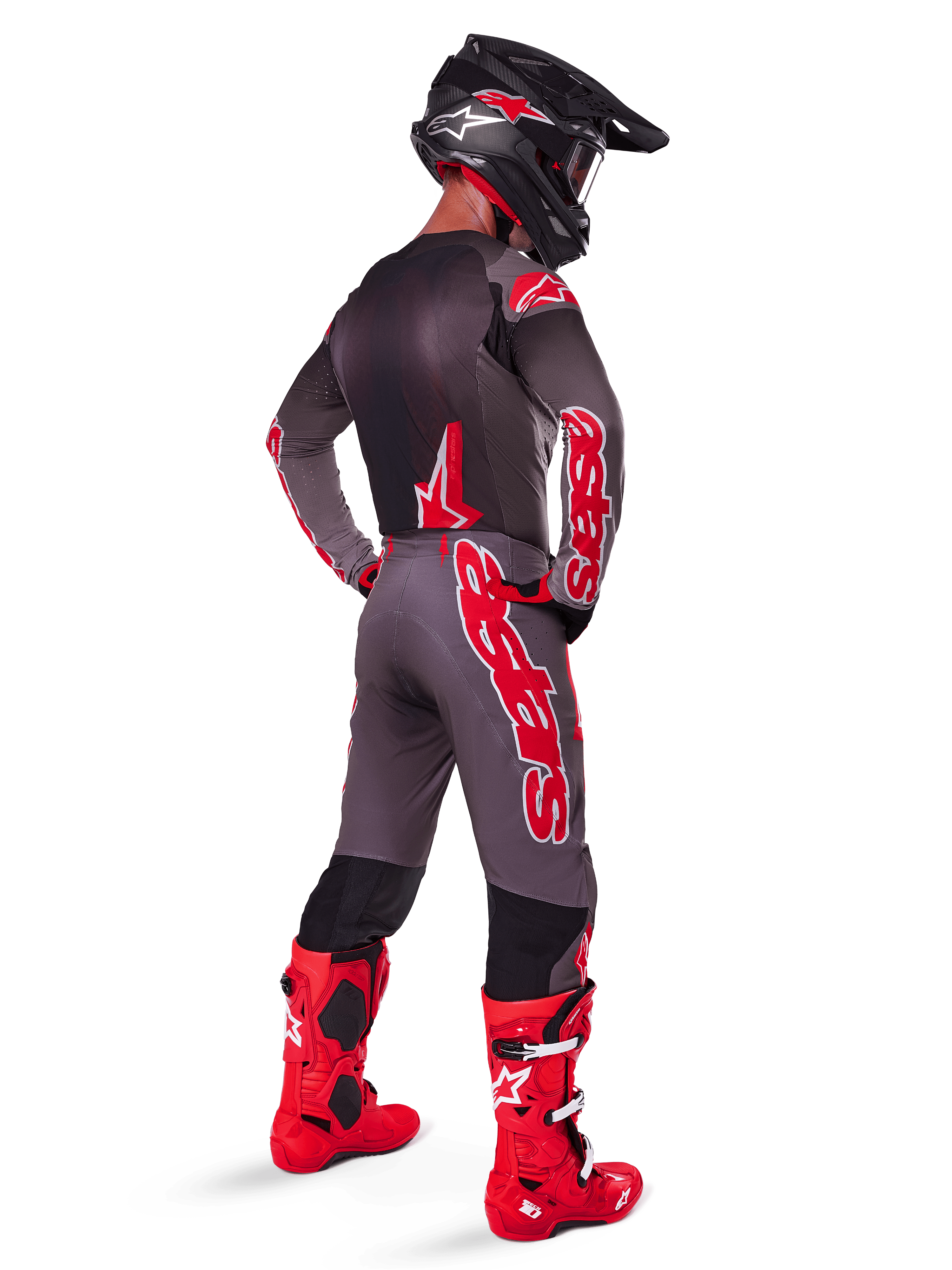 Motocross-Fahrer in Alpinestars 2025 Supertech Lipan Hose, Smoke Bright Red, graue Hose mit großen roten Logos und schwarzen Innenbein-Einsätzen, kombiniert mit passendem grauen Trikot, schwarzem Helm und leuchtend roten Stiefeln, komplettes Offroad-Rennoutfit in der Rückansicht.