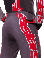 Alpinestars 2025 Supertech Lipan Hose, Motocross-Hose, Smoke Bright Red, Nahaufnahme der Rückansicht mit dunkelgrauem Gewebe und markanten roten Grafiken, getragen mit passenden roten und schwarzen Handschuhen und Trikot, mit Belüftungsperforationen und ergonomischen Nähten für Offroad-Performance