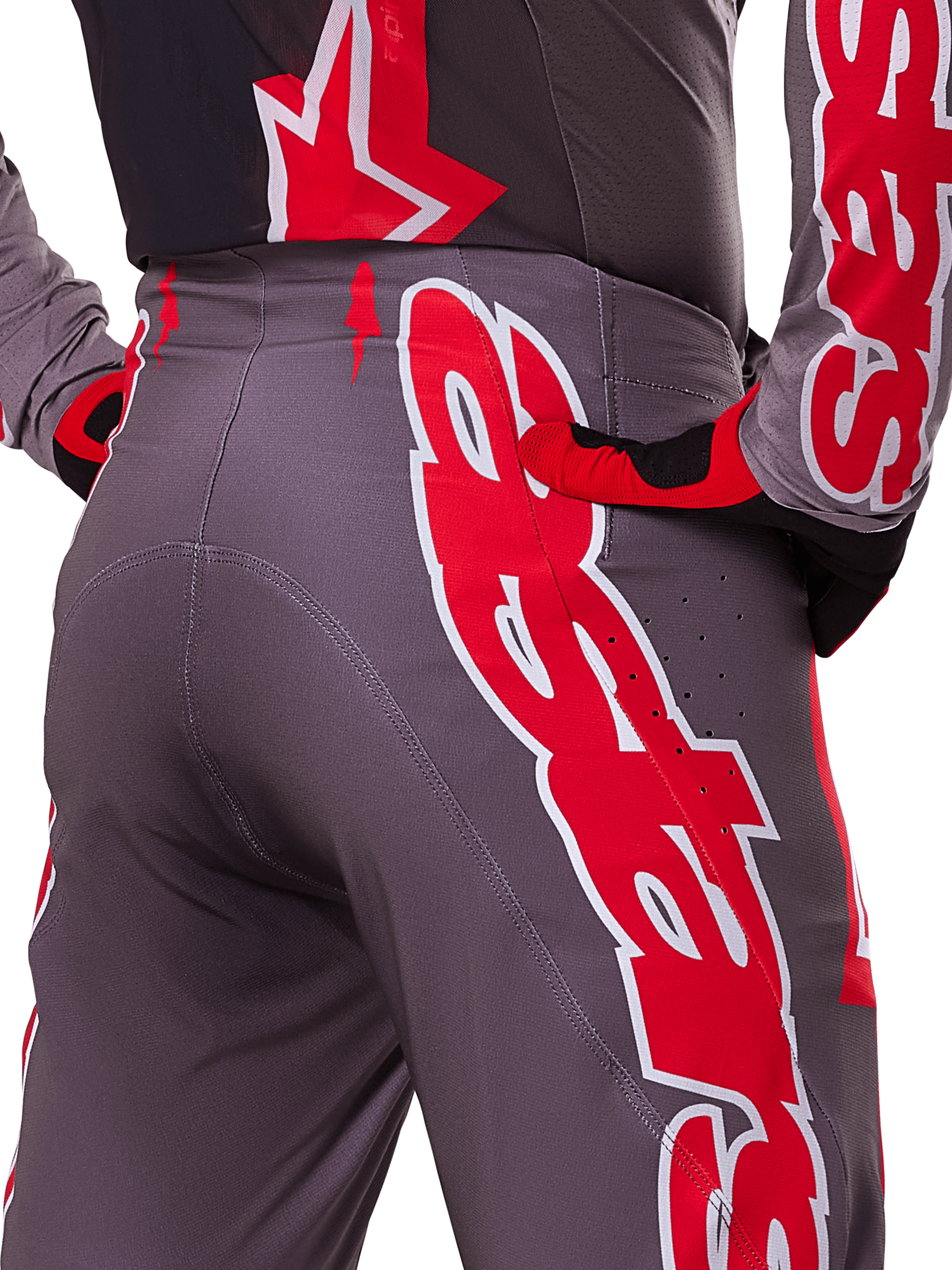 Alpinestars 2025 Supertech Lipan Hose, Motocross-Hose, Smoke Bright Red, Nahaufnahme der Rückansicht mit dunkelgrauem Gewebe und markanten roten Grafiken, getragen mit passenden roten und schwarzen Handschuhen und Trikot, mit Belüftungsperforationen und ergonomischen Nähten für Offroad-Performance