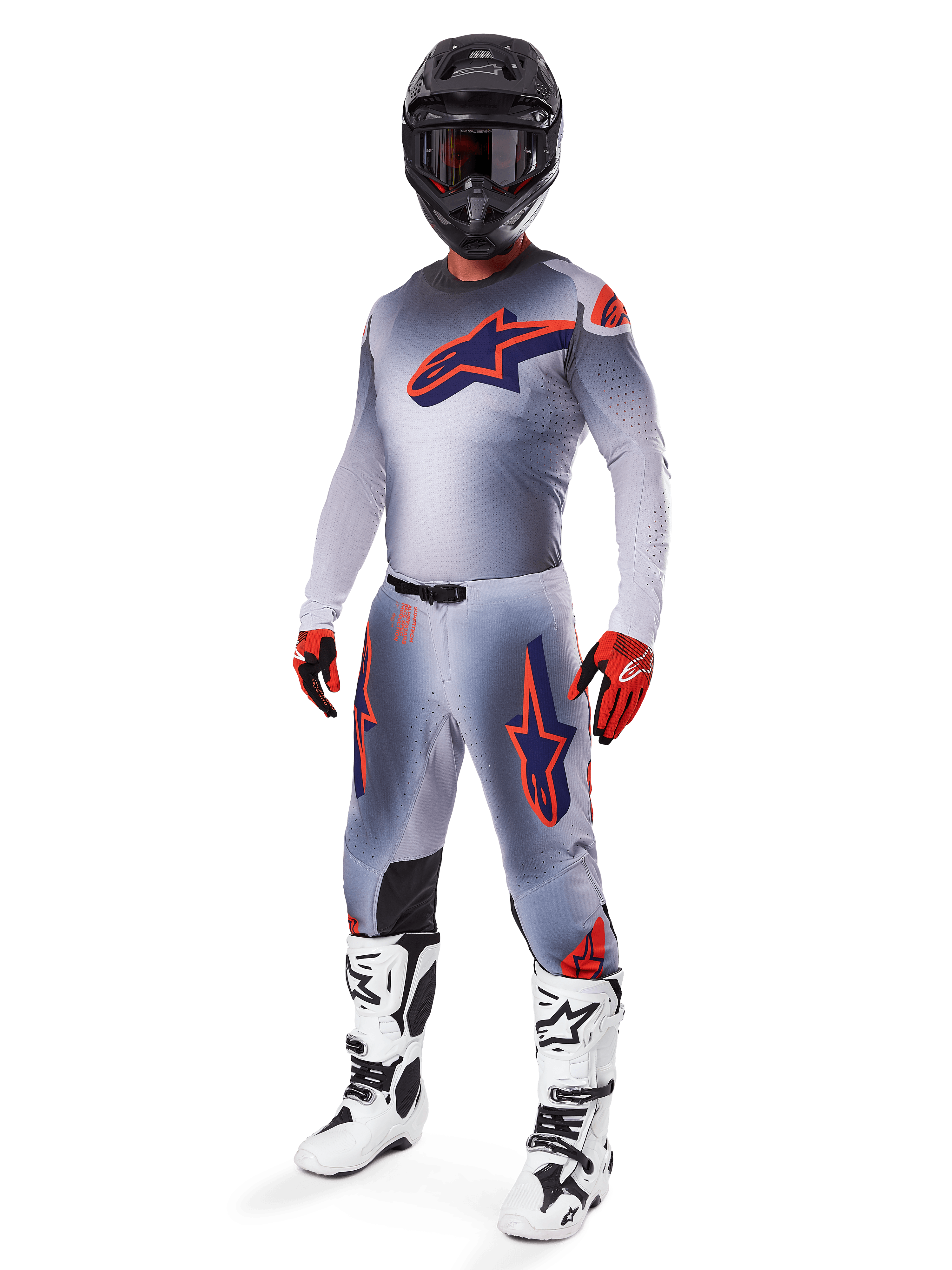 Motocross-Fahrer in kompletter Alpinestars 2025 Supertech Lipan Rennausrüstung, Grau und Orange Fluo, graues Trikot mit großem orangefarbenem Brustlogo, passende Hose mit orangefarbenen Akzenten, schwarzer Helm, rote Handschuhe und weiße Stiefel, professionelles Offroad-Rennoutfit
