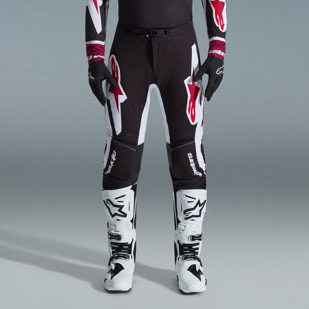 Alpinestars 2026 Supertech AFD Vista Ausrüstungsset, Motocross-Fahrer mit schwarzer Hose und großen weißen und roten Logos, passendes Performance-Jersey mit burgunderroten Bündchen, schwarze Handschuhe und weiße Profi-Rennstiefel, Hochleistungs-Offroad-Rennausstattung