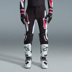 Alpinestars 2026 Supertech AFD Vista Ausrüstungsset, Motocross-Fahrer mit schwarzer Hose und großen weißen und roten Logos, passendes Performance-Jersey mit burgunderroten Bündchen, schwarze Handschuhe und weiße Profi-Rennstiefel, Hochleistungs-Offroad-Rennausstattung