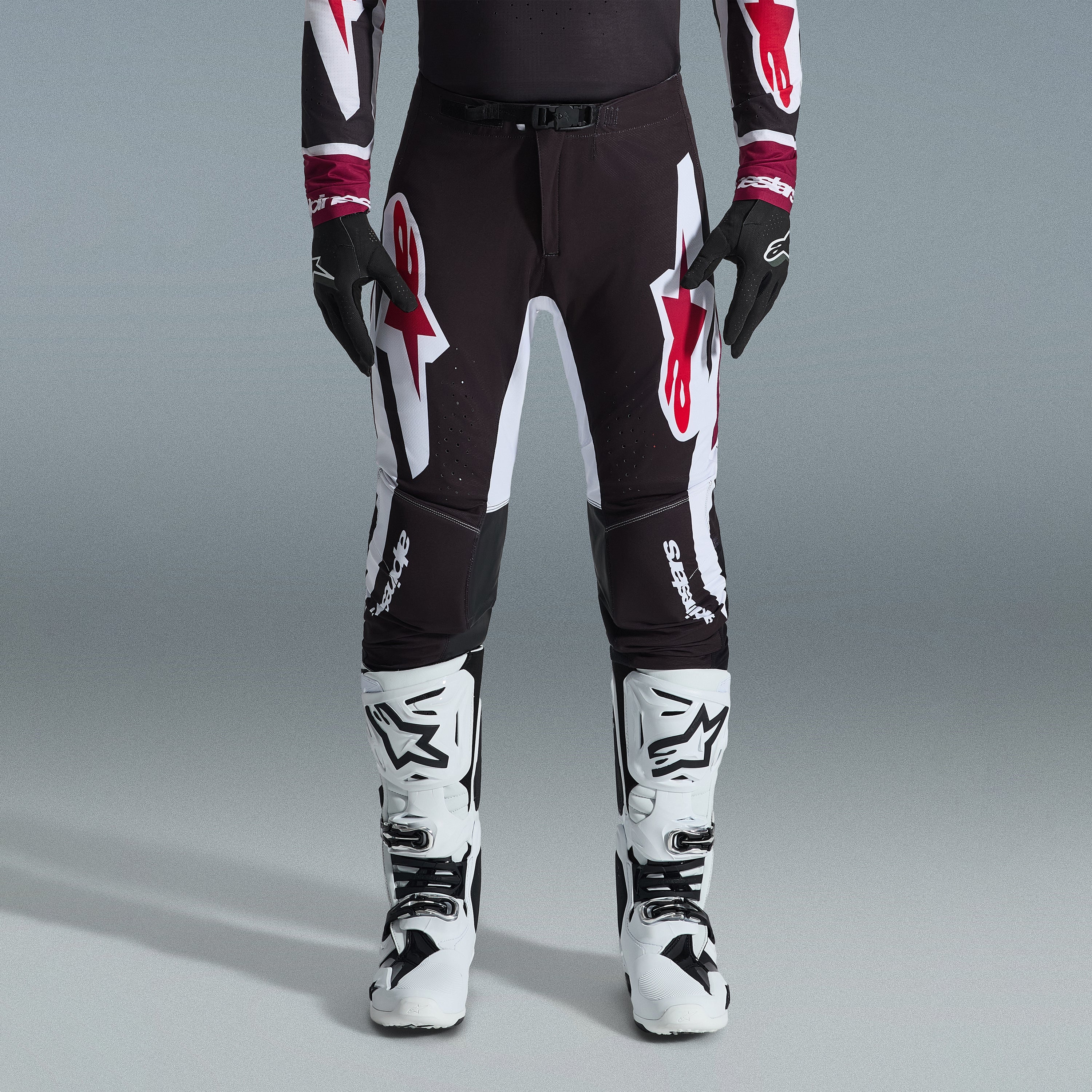 Alpinestars 2026 Supertech AFD Vista Ausrüstungsset, Motocross-Fahrer mit schwarzer Hose und großen weißen und roten Logos, passendes Performance-Jersey mit burgunderroten Bündchen, schwarze Handschuhe und weiße Profi-Rennstiefel, Hochleistungs-Offroad-Rennausstattung