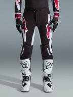 Alpinestars 2026 Supertech AFD Vista Pants, Motocross Pants, Black Red and White, featuring large graphic logos on the thighs and knees, worn with white racing boots and black gloves, athletic race-ready design for elite off-road competition