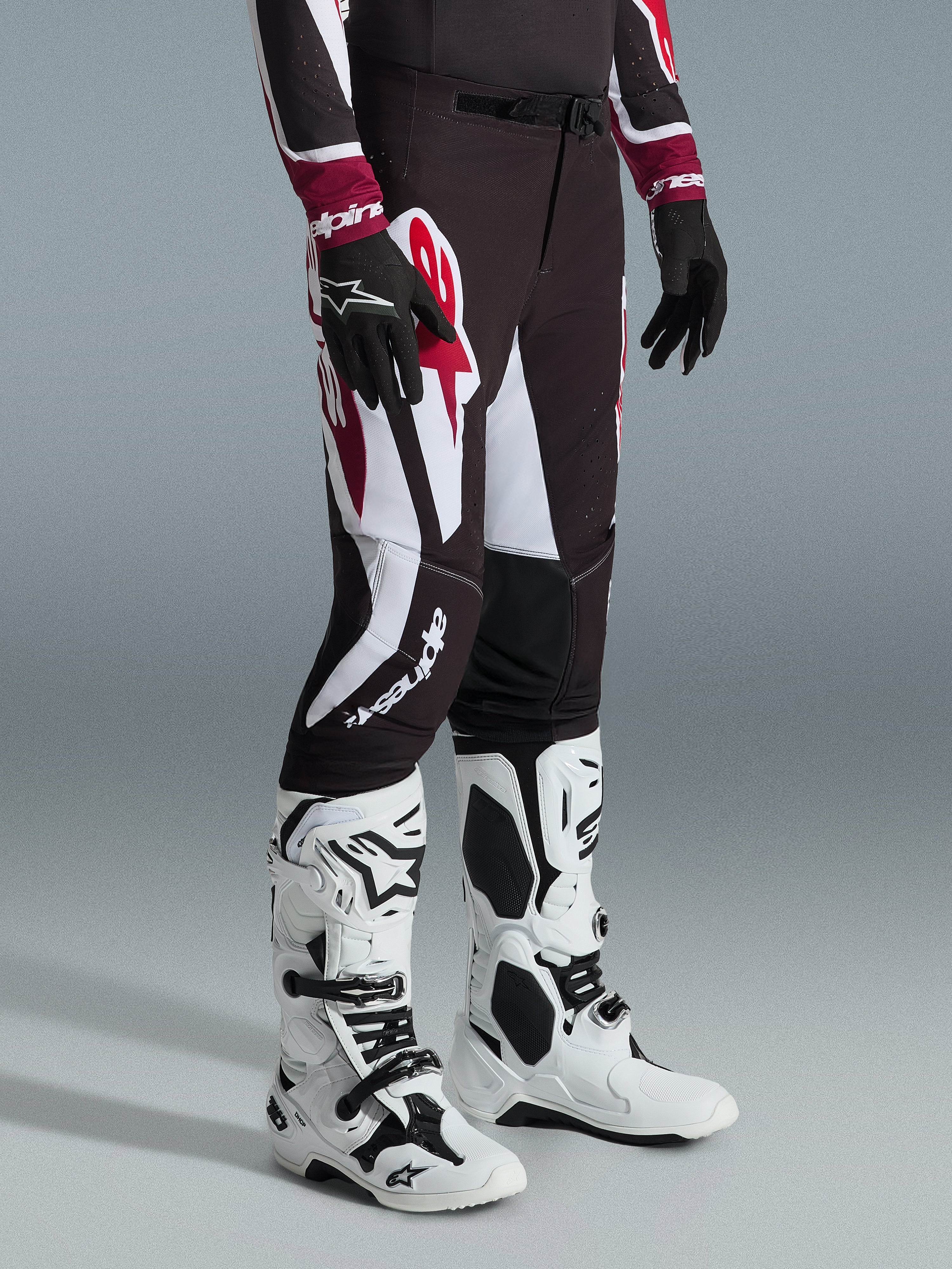 Alpinestars 2026 Supertech AFD Vista Hose, Motocross-Hose, Schwarz, Rot und Weiß, mit markanten grafischen Mustern und Branding, getragen mit weiß-schwarzen Offroad-Stiefeln und schwarzen Handschuhen, professionelle athletische Passform.