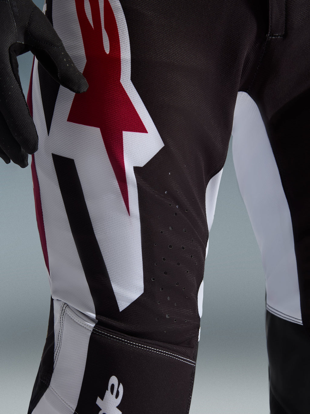 Alpinestars 2026 Supertech AFD Vista Hose, Motocross-Hose, Schwarz, Rot und Weiß, Nahaufnahme des Oberschenkels mit großem rot-weißem Astars-Logo und lasergeschnittenen Perforationen zur Belüftung.