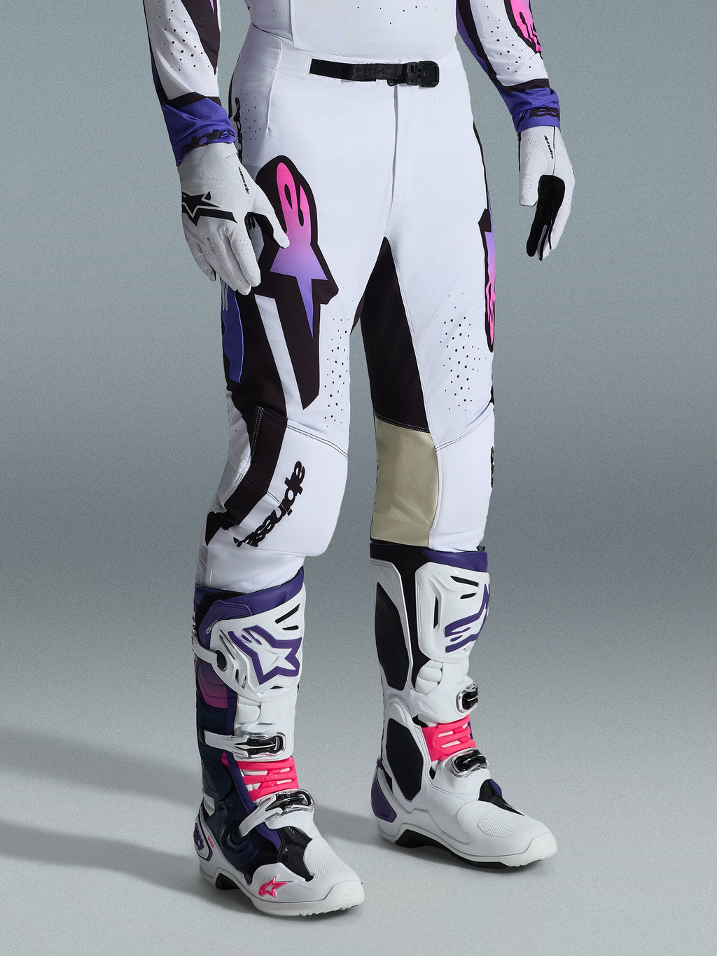 Alpinestars 2026 Supertech AFD Vista Hose, Motocross-Hose, Weiß, Lila und Schwarz, mit einem Astar-Logo mit pinkfarbenem und lila Farbverlauf, getragen mit passenden weiß-lila Motocross-Stiefeln und Handschuhen, athletische Rennpassform mit hellbraunen Leder-Innenknie-Paneelen und perforierten Details.
