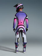 Motocross-Fahrer in der Rückansicht, komplette Rennausrüstung, Trikot mit lila-pinkem Farbverlauf, Alpinestars 2026 Supertech AFD Vista Hose in Weiß, Lila und Schwarz, schwarzer Helm mit lila Brille, weiß-lila Stiefel, farblich abgestimmtes Offroad-Rennset.