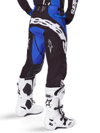 Alpinestars 2025 Techstar Dreem Hose, Motocross-Hose, Schwarz und Blau, Rückansicht mit markantem weißem Alpinestars-Schriftzug am Gesäß, kombiniert mit weiß-schwarzen Motocross-Stiefeln und passendem blauem Jersey, athletische Passform für den Offroad-Rennsport
