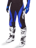 Alpinestars 2025 Techstar Dreem Hose, Motocross-Hose, Schwarz und Blau, getragen mit weißen Motocross-Stiefeln und blauen Handschuhen, mit weißem Alpinestars-Logo am Bein, strapazierfähige Konstruktion für Offroad-Rennsport