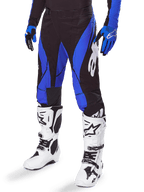 Alpinestars 2025 Techstar Dreem Hose, Motocross-Hose, Schwarz und Blau, getragen mit weißen Motocross-Stiefeln und blauen Handschuhen, mit weißem Alpinestars-Logo am Bein, strapazierfähige Konstruktion für Offroad-Rennsport