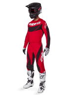 Motocross-Fahrer in kompletter Rennausrüstung mit Alpinestars 2025 Techstar Dreem Hose in Hellrot und Schwarz, passendes rot-schwarzes Trikot mit weißem Logo, schwarzer Helm und weiß-schwarze Stiefel, abgestimmtes Outfit für Offroad-Rennen