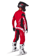 Alpinestars 2025 Techstar Dreem Hose, Motocross-Hose, Hellrot und Schwarz, von einem Fahrer aus der Rückansicht in kompletter Rennausrüstung getragen, mit passendem rotem Trikot, schwarzem Helm und weißen Stiefeln, markantes weißes Alpinestars-Branding und schwarze Stretch-Einsätze.