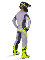 Motocross rider seen from behind wearing full racing gear, including Alpinestars 2025 Techstar Dreem Pants in Gray and Dark Gray with bold neon yellow accents, matching gray jersey with neon graphics, bright neon yellow boots, and black helmet, coordinated professional motocross outfit