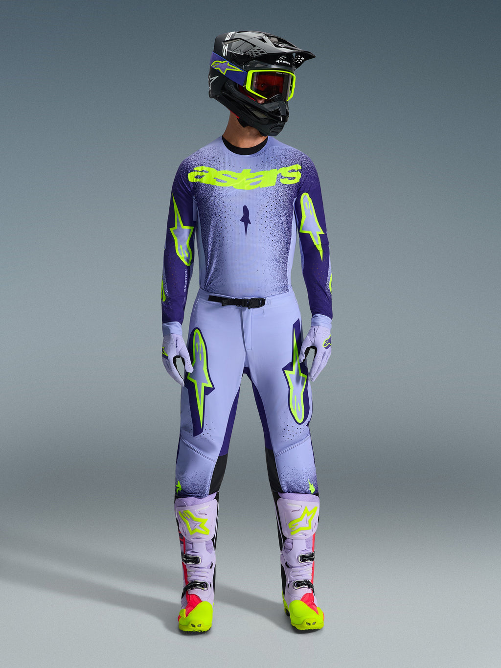 Alpinestars 2026 Supertech Scenz Hose, Motocross-Hose, Purple Yellow Fluo, getragen als komplettes Rennbekleidungsset mit passendem lavendelfarbenem Trikot, Handschuhen und Stiefeln, mit markanten neongelben Logos, athletische Passform für professionellen Offroad-Rennsport.