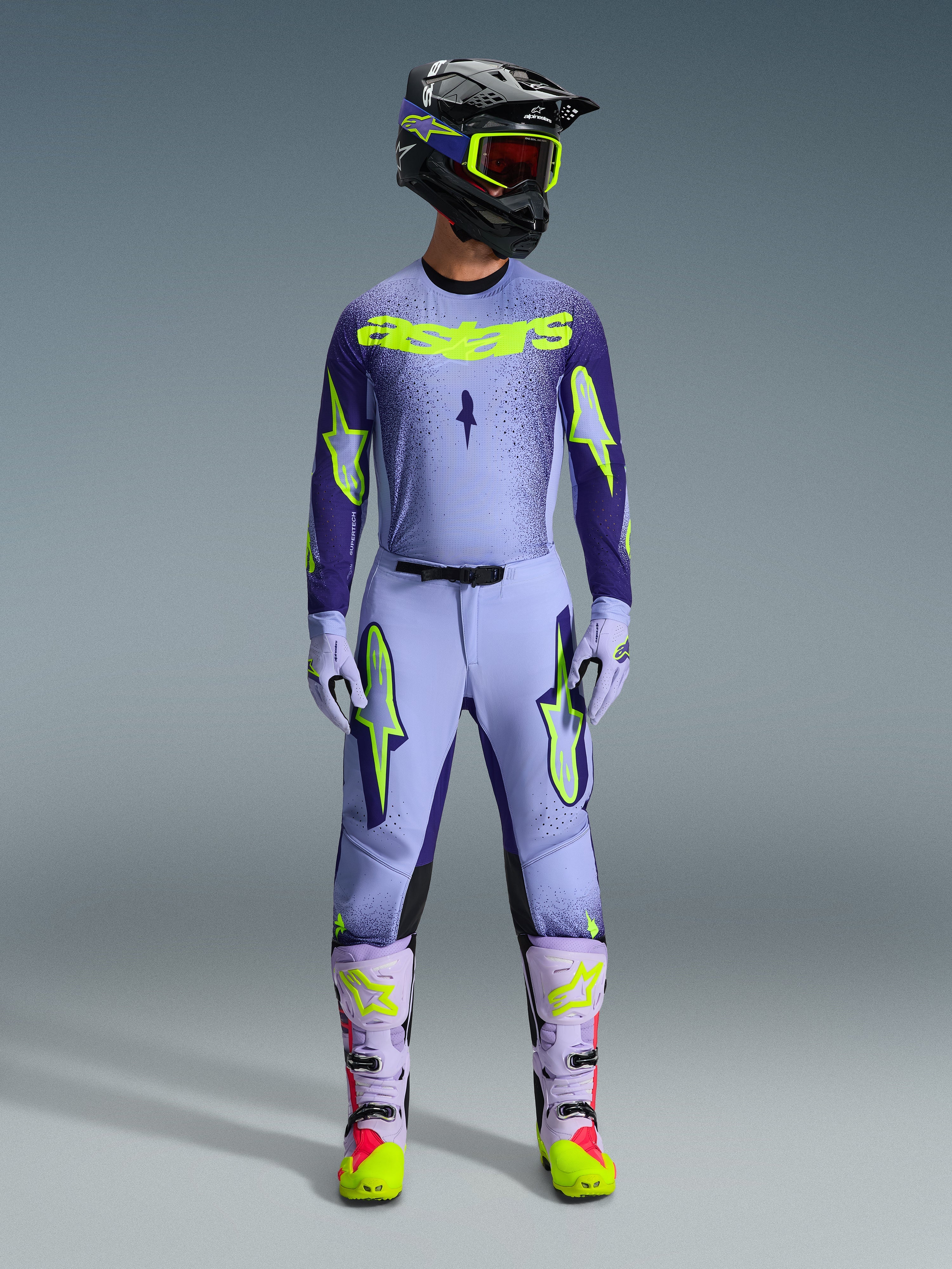 Alpinestars 2026 Supertech Scenz Hose, Motocross-Hose, Purple Yellow Fluo, getragen als komplettes Rennbekleidungsset mit passendem lavendelfarbenem Trikot, Handschuhen und Stiefeln, mit markanten neongelben Logos, athletische Passform für professionellen Offroad-Rennsport.