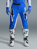 Alpinestars 2026 Supertech Scenz Hose, Motocross-Hose, Ucla Blau Weiß, getragen mit passenden blauen Handschuhen und weißen Stiefeln, mit großen weiß-schwarzen Grafiken auf den Oberschenkeln, athletische Passform für Offroad-Performance