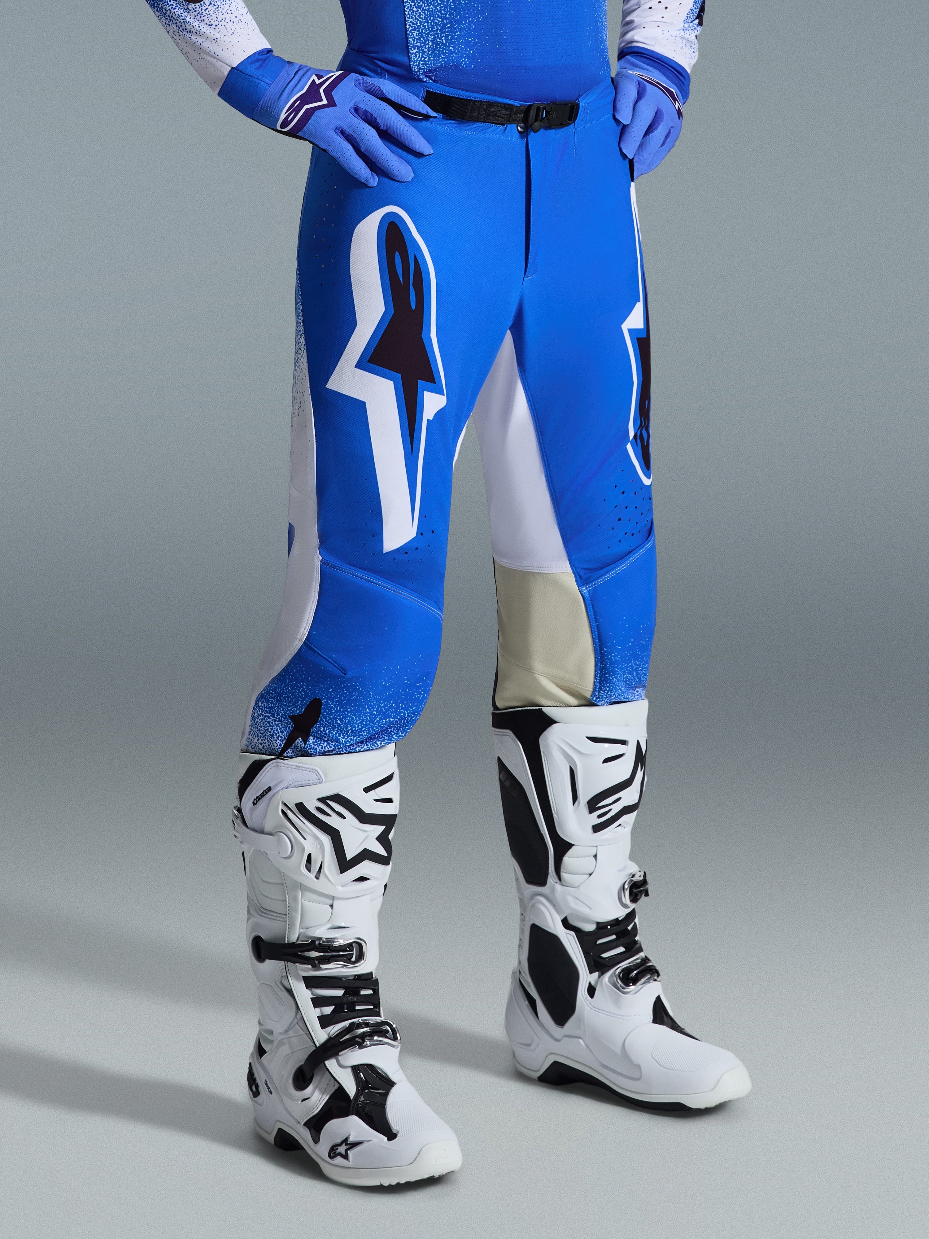 Alpinestars 2026 Supertech Scenz Hose, Motocross-Hose, Ucla-Blau und Weiß, getragen mit weiß-schwarzen Stiefeln und blauen Handschuhen, mit großen Grafik-Logos an den Oberschenkeln und weißen Einsätzen, athletische Passform für professionelles Motocross-Fahren