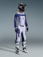 Motocross-Fahrer in der 2026 Supertech Scenz Hose in Hellgrau und Dunkelblau, passendes blau-weißes Trikot mit „astars“-Branding und Spray-Effekt, schwarzer Helm mit weißer Schutzbrille, weiß-schwarze Motocross-Stiefel, koordinierte professionelle Offroad-Rennausrüstung.