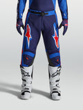 Alpinestars Racer Hunt Hose, Motocross-Hose für Herren, Blau und Rot, strapazierfähige Konstruktion mit auffälligen Sterngrafiken, getragen mit weißen Stiefeln.