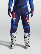 Alpinestars Racer Hunt Hose, Motocross-Hose für Herren, Blau und Rot, strapazierfähige Konstruktion mit auffälligen Sterngrafiken, getragen mit weißen Stiefeln.