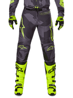 Alpinestars 2025 Racer Hollow Hose, Motocross-Hose, Dunkelgrau mit Neongelb, Sterndesigns und Logo, Person trägt komplette Offroad-Schutzausrüstung mit schwarzen und neongelben Handschuhen und neongelben Stiefeln
