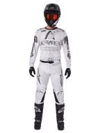 Motocross rider wearing the Alpinestars 2025 Racer Hollow Pants in Light Camo Brown, paired with a matching white and grey long-sleeve jersey, black helmet with orange-red goggles, black gloves, and black boots, coordinated racing gear set for off-road performance.