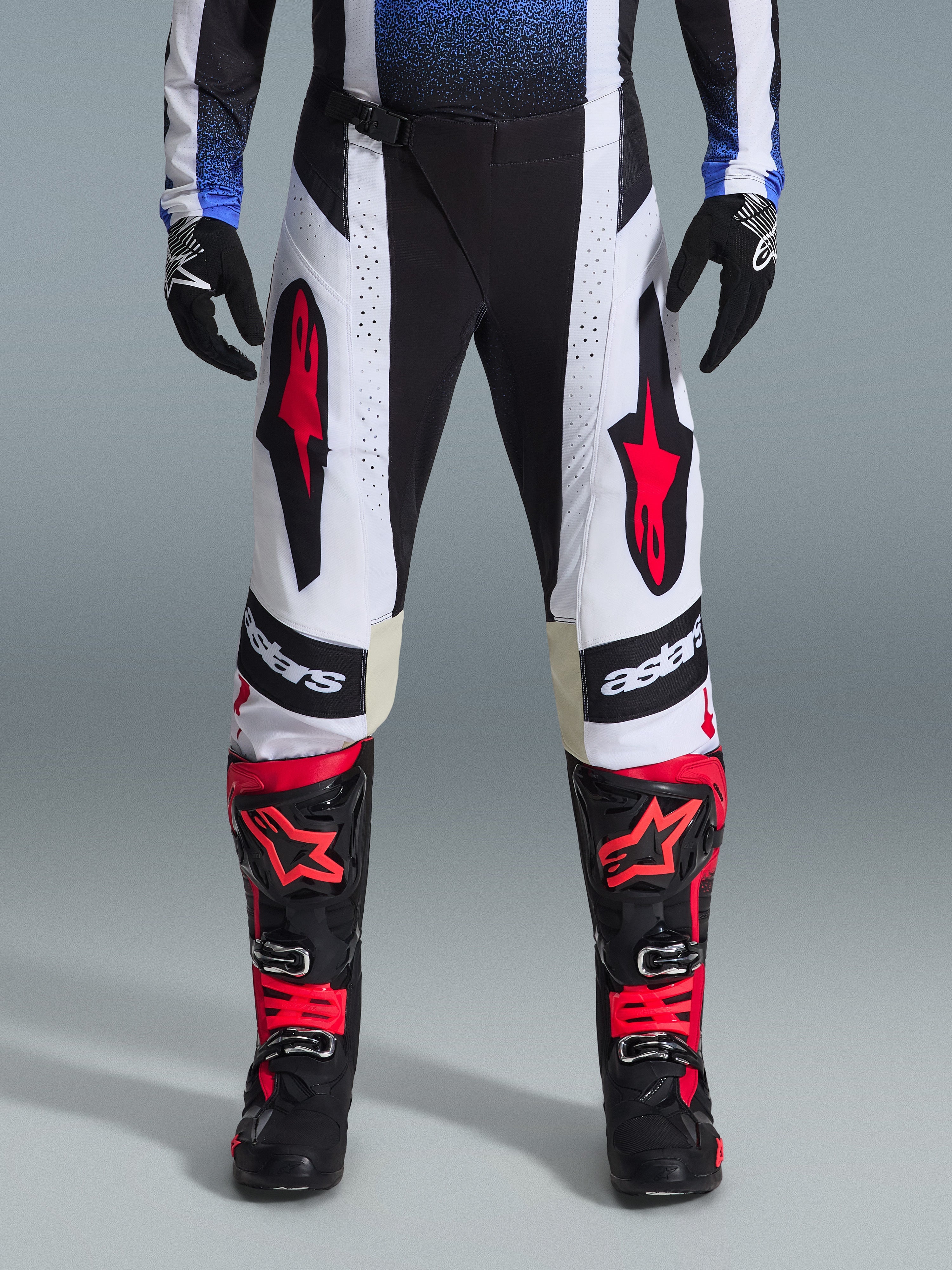 Alpinestars 2026 Techstar Knif Hose, Motocross-Hose, Schwarz, Weiß und Rot, getragen mit passenden rot-schwarzen Stiefeln und schwarzen Handschuhen, mit markanten roten Stern-Logos auf weißen Einsätzen und technischen perforierten Details für den Offroad-Rennsport.