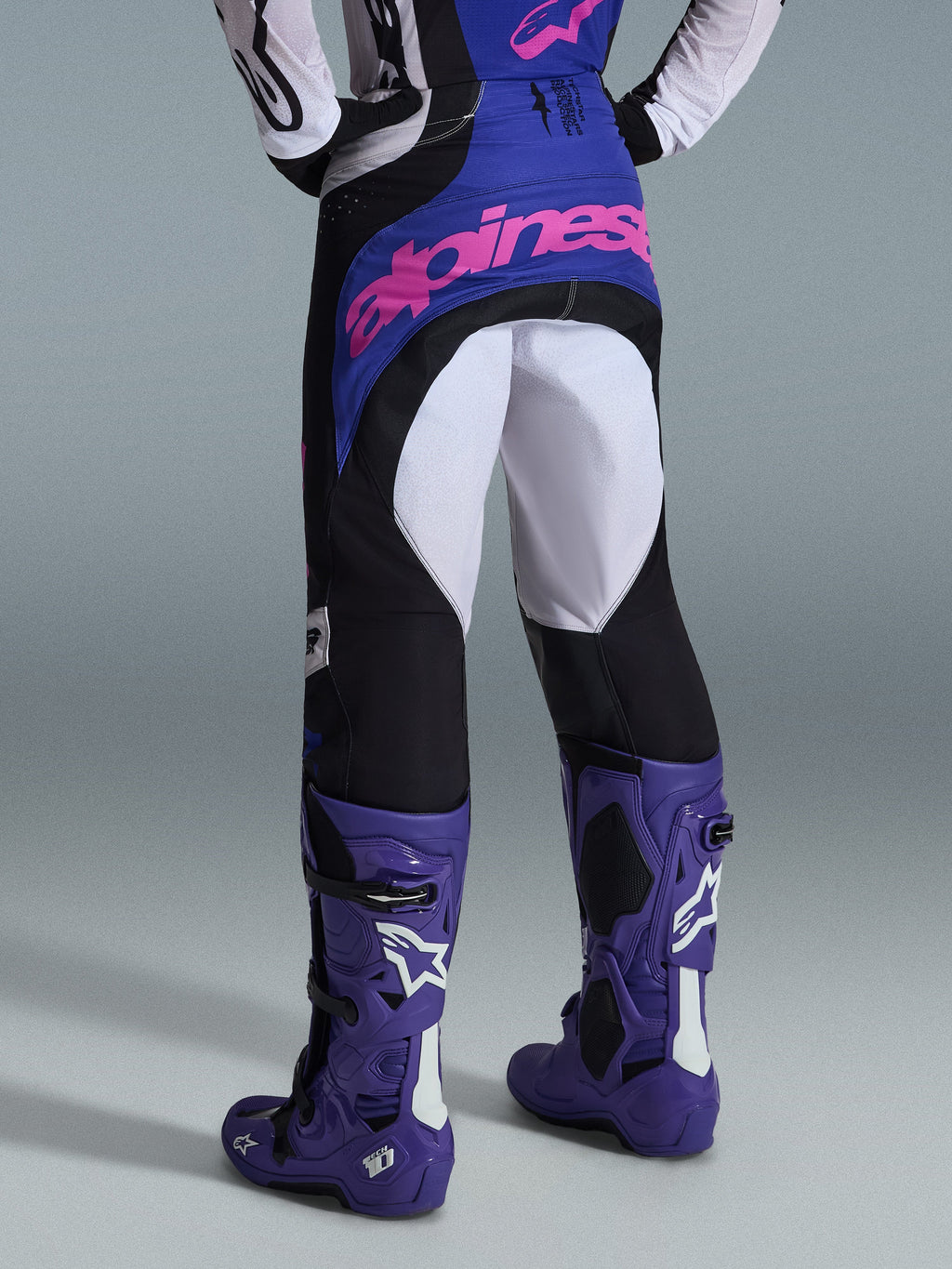 Alpinestars 2026 Techstar Knif Pants, Motocross Pants, Black Light Gray and Purple, rear view featuring pink branding on the seat, worn with matching jersey and purple motocross boots, professional off-road racing outfit