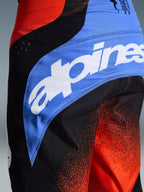 Nahaufnahme der Alpinestars 2026 Techstar Knif Hose, Motocross-Hose, Orange, Schwarz und UCLA Blue, mit großem weißem Alpinestars-Logo auf einem blauen Seiteneinsatz, technisches Gewebe mit orangefarbenem Farbverlauf, athletische Rennpassform für Offroad-Performance