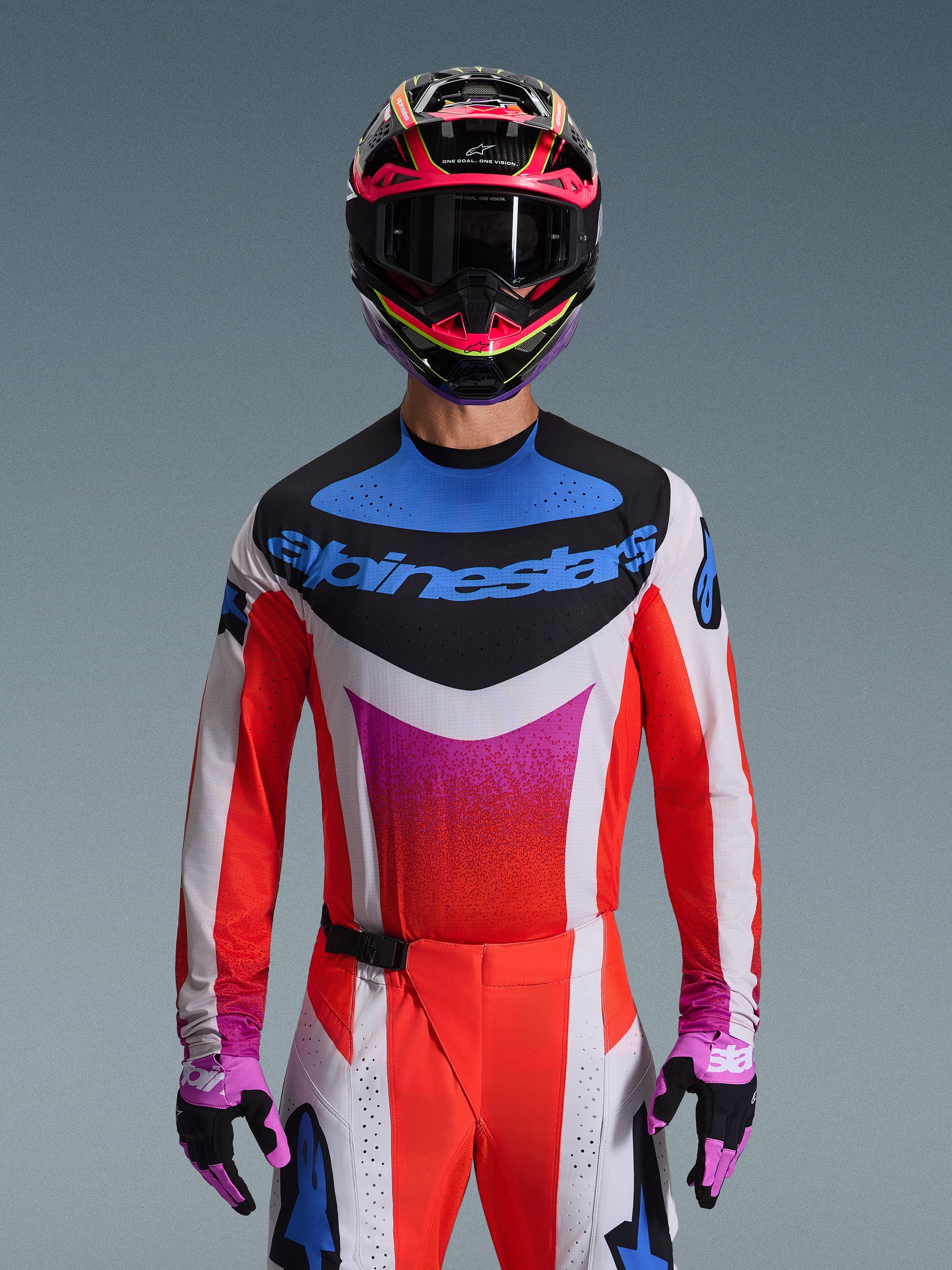 Motocross-Fahrer im Alpinestars 2026 Techstar Knif Trikot in Hellgrau Orange Fluo Schwarz, markantes blaues Logo und leuchtend orangefarbene Ärmel, kombiniert mit pink-schwarzem Helm und lila Handschuhen, athletische Rennpassform für professionelle Offroad-Wettkämpfe