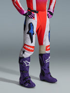 Alpinestars 2026 Techstar Knif Hose, Motocross-Hose, Weiß und leuchtendes Rot mit blauen Grafikakzenten, mit einem „astars“-Logo am Knie, getragen mit lila Stiefeln und schwarz-pinken Handschuhen, professionelles Offroad-Rennsport-Set