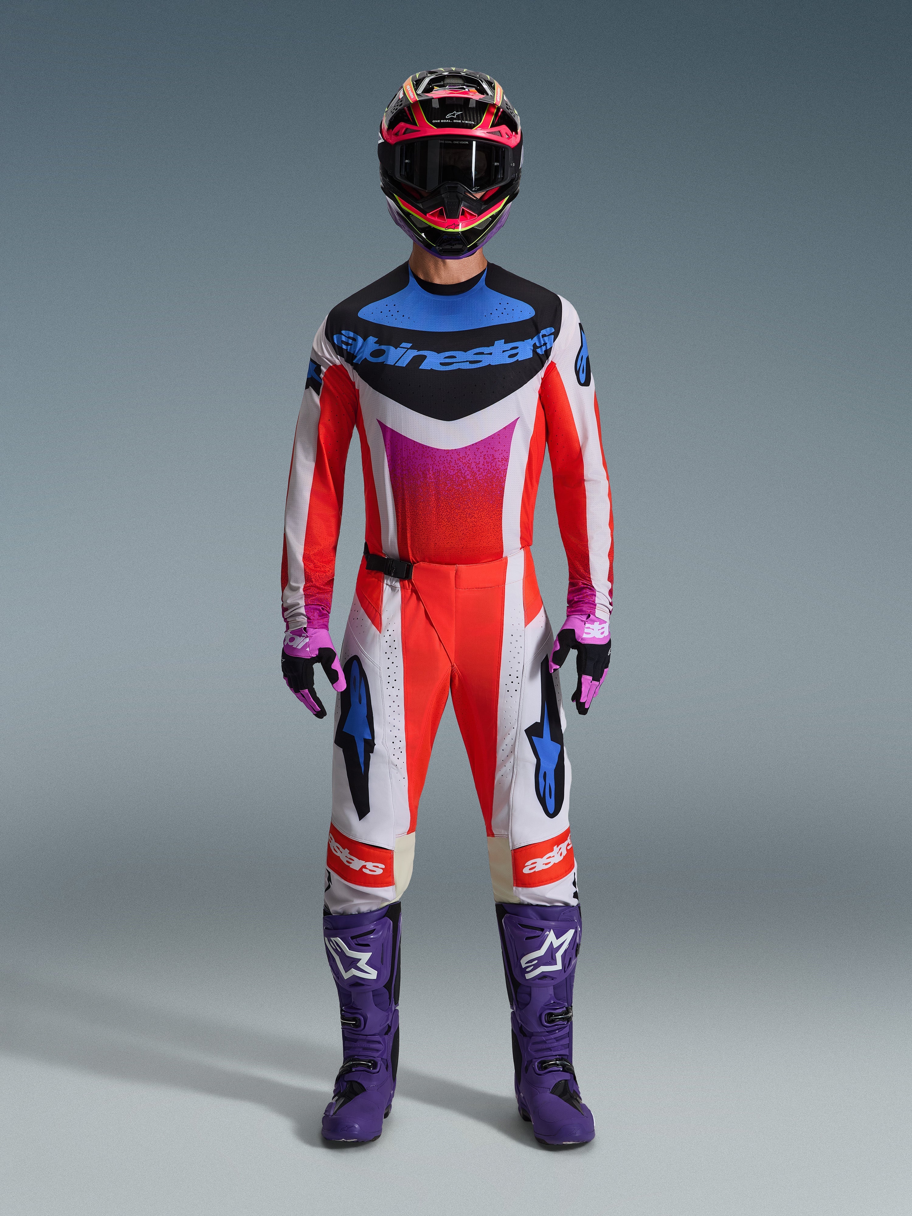 Motocross-Fahrer im 2026 Techstar Knif Gear Set, komplette Rennausrüstung in Rot, Weiß und Schwarz mit blauem Branding und rosa Akzenten, lila Stiefel mit weißen Logos, rosa-schwarze Handschuhe und ein schwarz-rosa Helm, professionelle Offroad-Ausrüstung