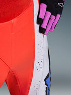Alpinestars 2026 Techstar Knif Hose, Motocross-Hose, Orange Fluo und Hellgrau mit blauen Akzenten, Nahaufnahme der lasergeschnittenen Belüftungsperforationen am Oberschenkel, kombiniert mit einem schwarz-lila Motocross-Handschuh