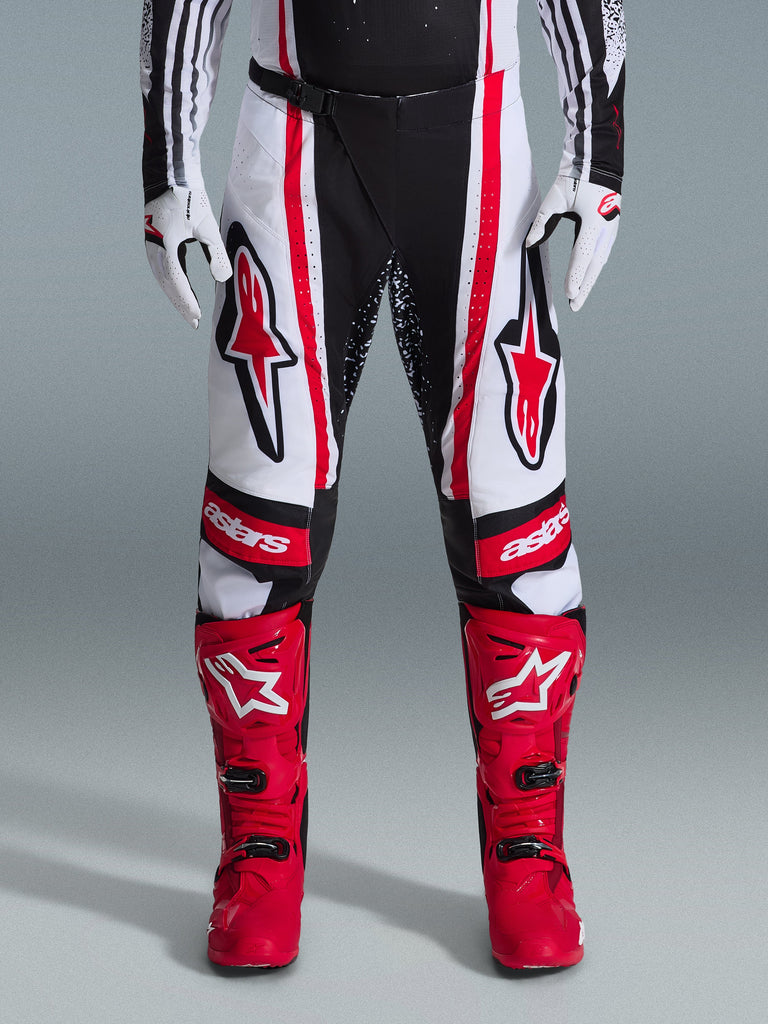 Alpinestars 2026 Techstar Nomur Hose, Motocross-Hose, Schwarz, Weiß und Rot, getragen mit passenden roten Stiefeln und weißen Handschuhen, markante rote Logos auf den Oberschenkeln und „astars“-Branding auf den Knien, Multi-Panel-Racing-Design für Offroad-Performance