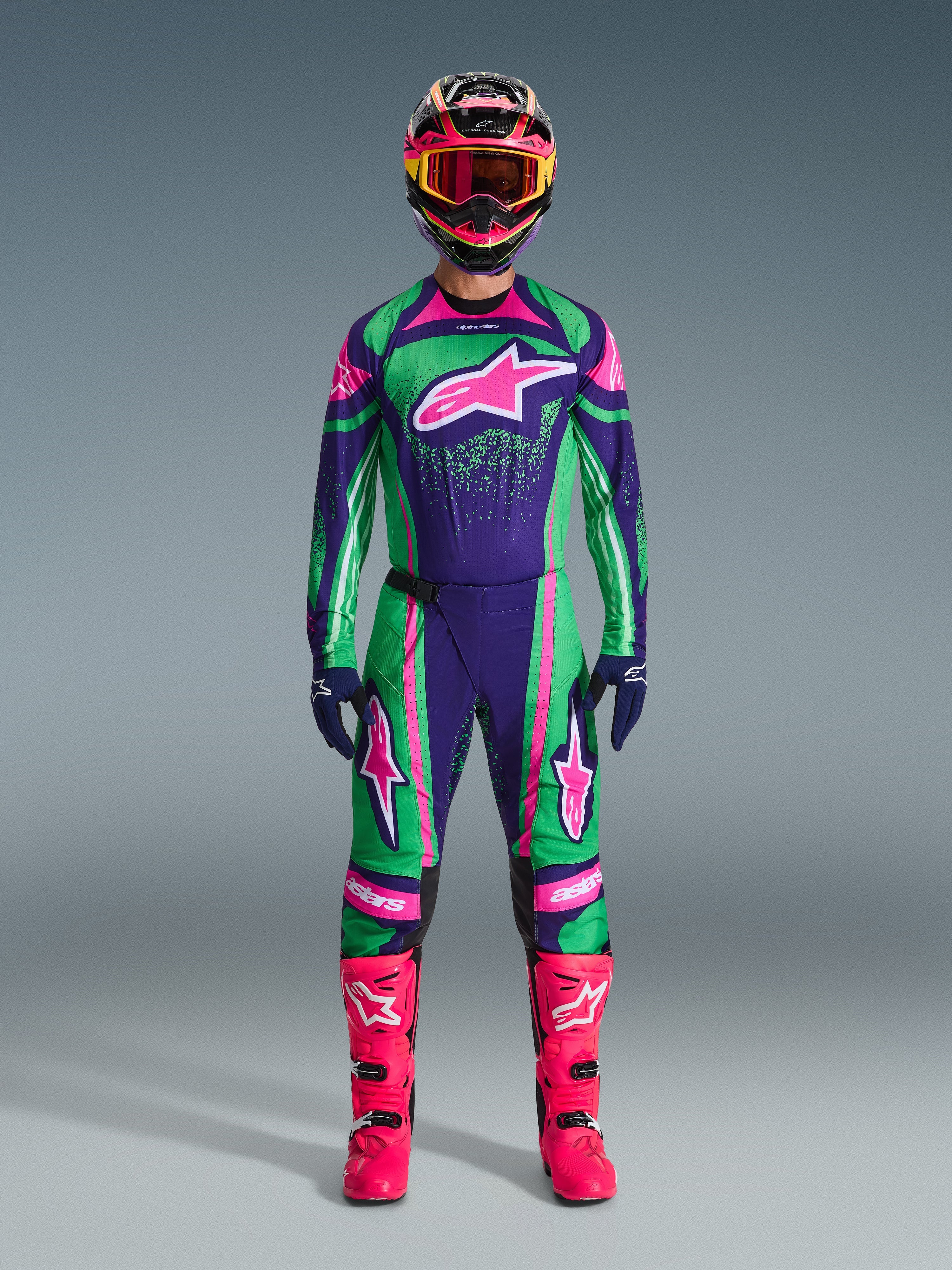 Alpinestars 2026 Techstar Nomur Gear Set, Motocross-Rennausrüstung, kräftiges Grün, Lila und Pink, großes Stern-Logo auf der Brust und den Oberschenkeln, schwarzer Helm mit pinken und gelben Akzenten, leuchtend pinke Stiefel, professionelles sportliches Design