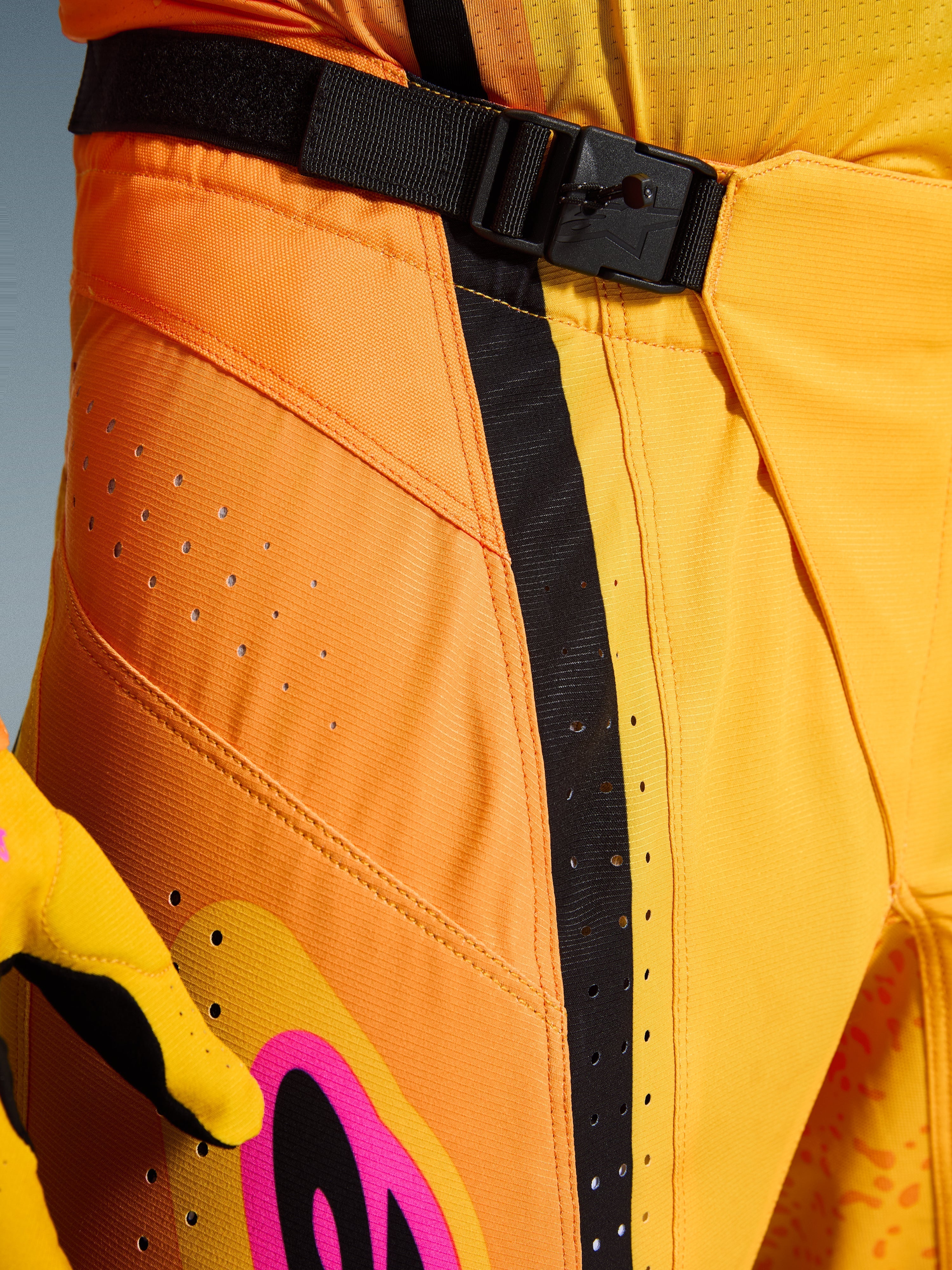 Alpinestars 2026 Techstar Nomur Hose, Motocross-Hose, Orange, Gelb, Pink, Nahaufnahme des Taillenbereichs mit dem SX2-Magnetverschluss, schwarzem Verstellriemen und lasergeschnittenen Belüftungsperforationen auf strapazierfähigem Ripstop-Material