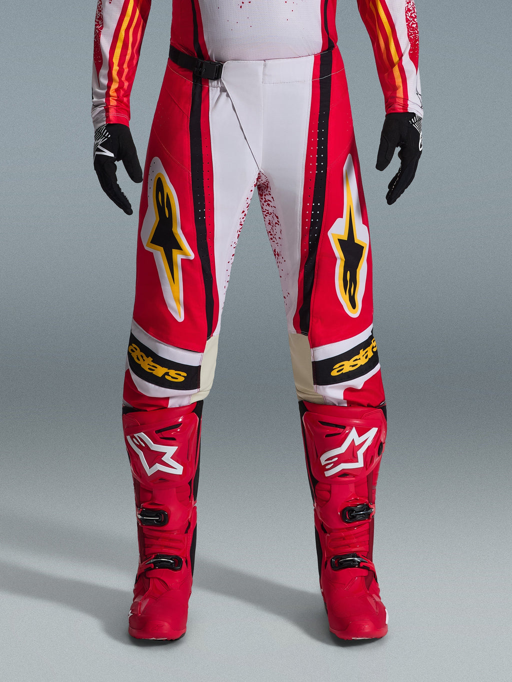 Alpinestars 2026 Techstar Nomur Hose, Motocross-Hose, Rot und Weiß mit schwarzen und gelben Akzenten, getragen mit passenden roten Stiefeln und schwarzen Handschuhen, leistungsstarke Offroad-Rennausrüstung