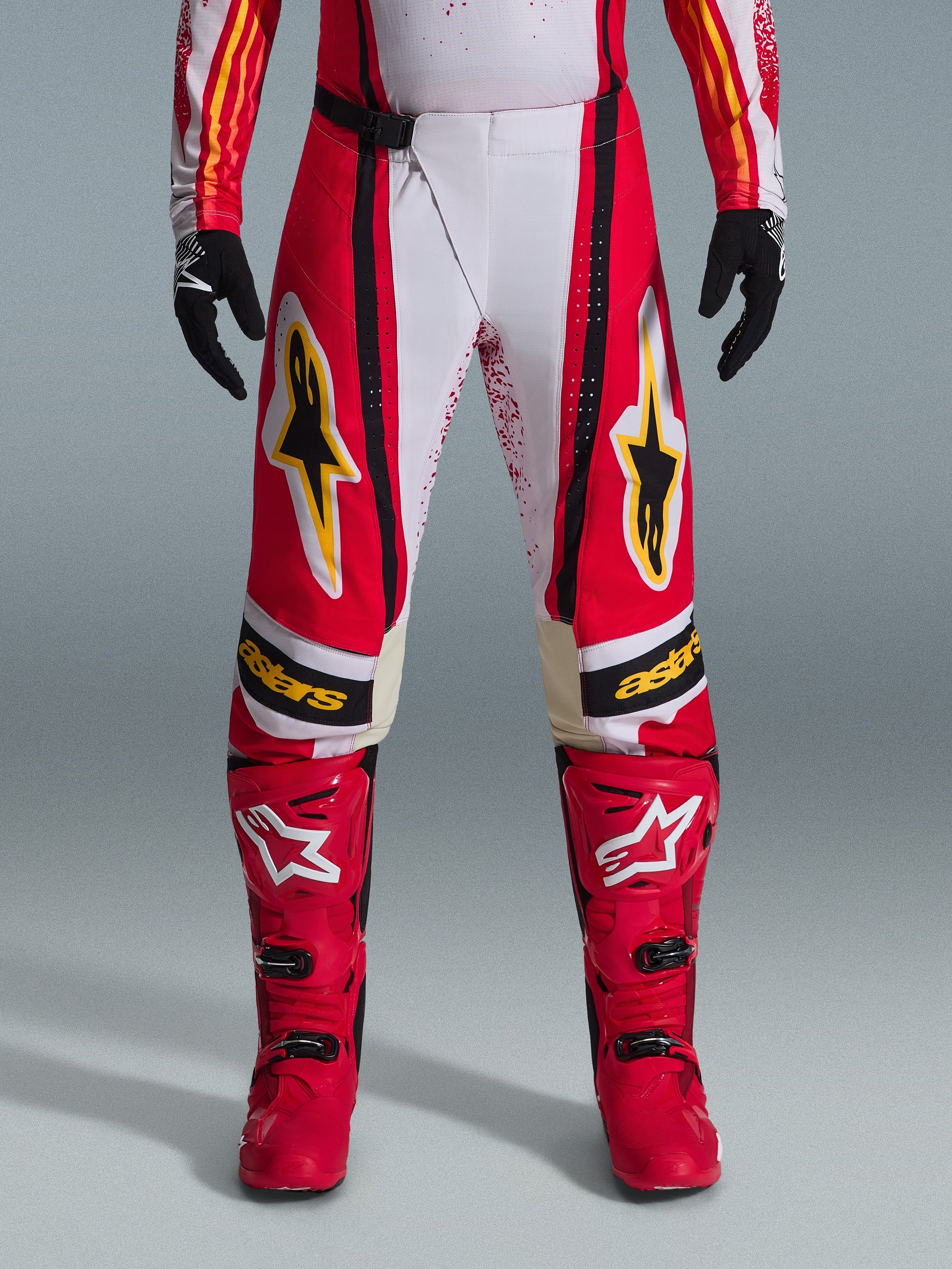 Alpinestars 2026 Techstar Nomur Hose, Motocross-Hose, Rot und Weiß mit schwarzen und gelben Akzenten, getragen mit passenden roten Stiefeln und schwarzen Handschuhen, leistungsstarke Offroad-Rennausrüstung