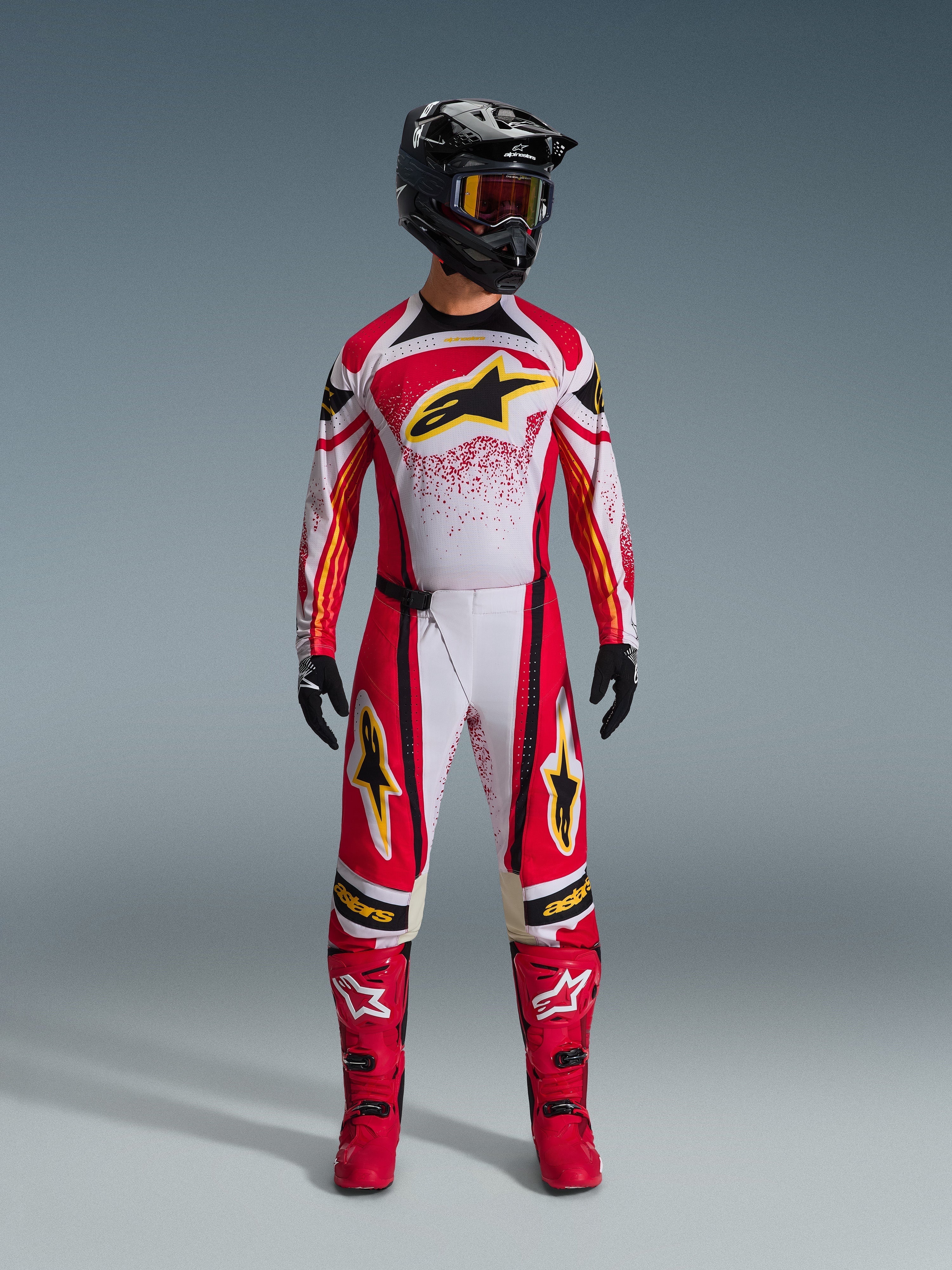 Alpinestars 2026 Techstar Nomur Trikot, Rot und Weiß mit schwarzen Akzenten und gelben Logos, getragen von einem Motocross-Fahrer mit passender Hose, roten Stiefeln und einem schwarzen Helm, professionelle Offroad-Rennausrüstung
