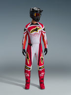 Motocross-Fahrer in Alpinestars 2026 Techstar Nomur Hose, rot-weiß-schwarze Offroad-Rennausrüstung, passendes Trikot mit gelbem Stern-Logo, schwarzer Helm mit Goggles, rote Stiefel und schwarze Handschuhe, abgestimmtes Outfit für Motocross