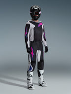 Motocross-Fahrer in kompletter Rennausrüstung, Alpinestars 2026 Fluid Grid Hose in Schwarz, Hellgrau und Lila, passendes Jersey mit pinken und blauen Grafiken, schwarzer Helm und Brille, weiße und schwarze Stiefel sowie schwarze Handschuhe, koordiniertes Outfit für den Offroad-Rennsport