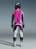 Motocross-Fahrer in der Rückansicht mit Alpinestars 2026 Fluid Grid Hose und passendem Trikot, Pink, Weiß und Schwarz mit violettem Branding, schwarzer Helm, weiß-schwarze Stiefel, abgestimmtes Rennoutfit für Offroad-Motocross