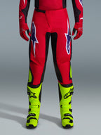 Alpinestars 2026 Fluid Grid Hose, Motocross-Hose, Rot mit schwarzen Einsätzen und neongelben Akzenten, mit großen weiß-violetten Stern-Logos auf den Oberschenkeln, getragen mit roten Handschuhen und neongelben Stiefeln, strapazierfähige Konstruktion für den Offroad-Rennsport